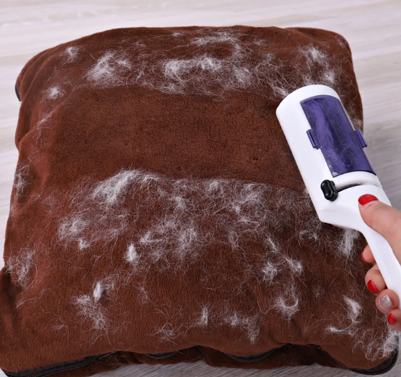 Reusable white and purple pet hair remover brush lifting fur from a brown cushion